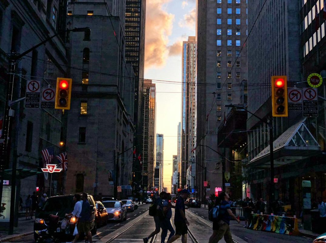 Pedestrians crossing a busy downtown Toronto street at golden hour